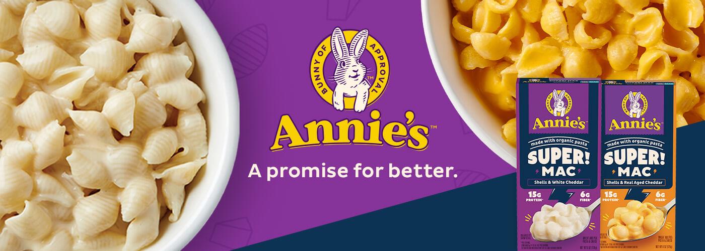 Two front facing pack shots of Super Mac Shells & White Cheddar and Shells Real-Aged Cheddar in the bottom right corner on a purple background with a bunny logo, two white bowls with Shells Mac in them and text in the middle has the Annies logo that says, "Annies's A promise for better."