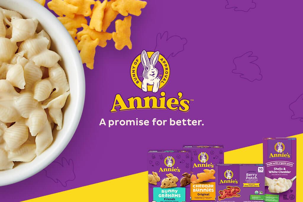 Four front facing pack shots of Bunny Grahams, Cheddar Bunnies, Fruit Snacks Berry Patch and Shells White Cheddar in the bottom right corner on a purple & yellow background with a bunny logo & text saying, "A promise for better". A white bowl of White Shells Cheddar Mac & Cheese and Cheddar Bunnies on the left side.