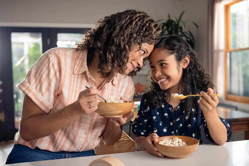 Mother and daughter enjoying Annie’s Mac and Cheese together, each holding a spoon and smiling at each other.