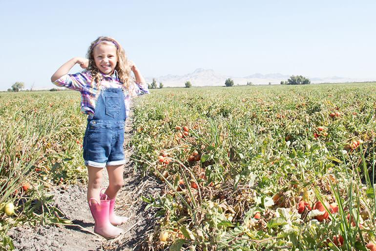 A young girl in a bodybuilder pose standing in a field.