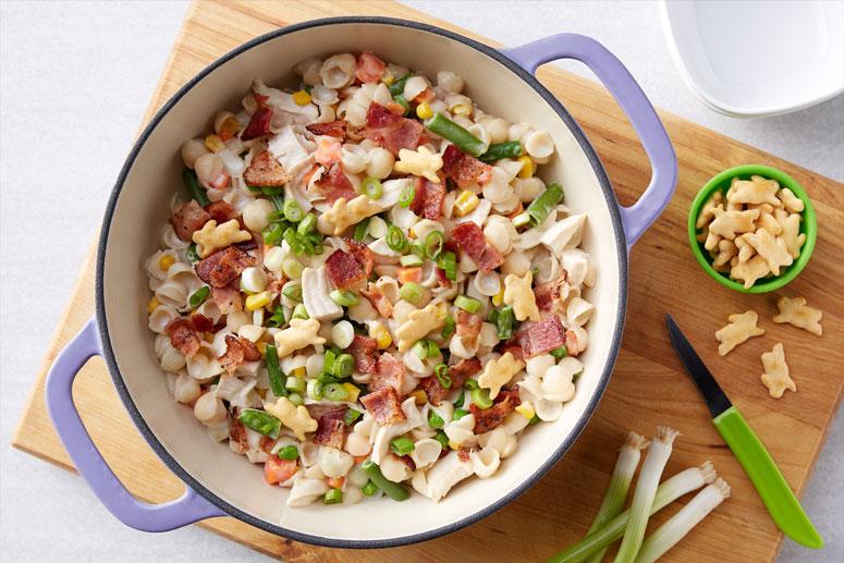 A large purple crock of Chicken-Bacon Shells & Cheese and a smaller bowl of individual Annie's Organic White Cheddar Bunnies Baked Crackers.