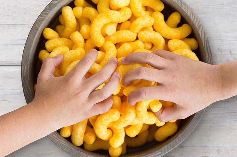 Two hands reaching into a bowl of Cheddar Cheesy Smiles.