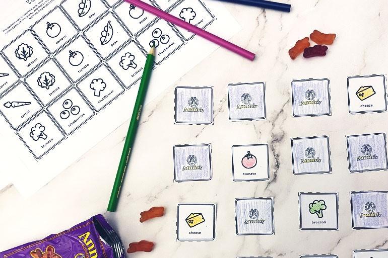 Lifestyle image showing a colored and cut out Annie's matching activity with some Fruit Snacks spilling out of a bag and colored pencils.