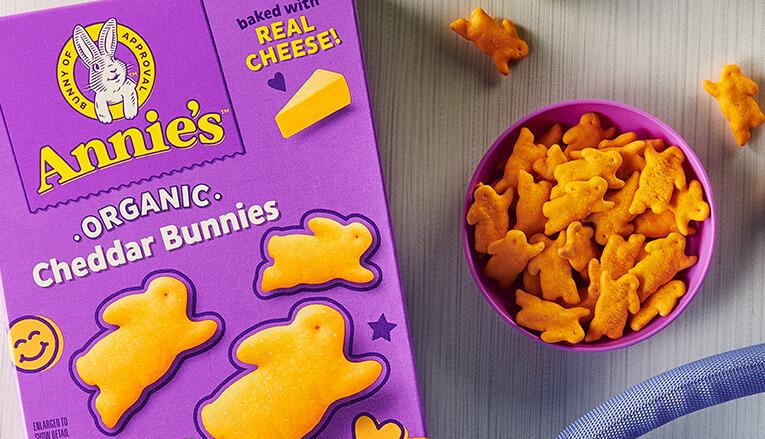 A close up photo of a package front of Annie's Organic Cheddar Bunnies product and a bowl of the next to it.