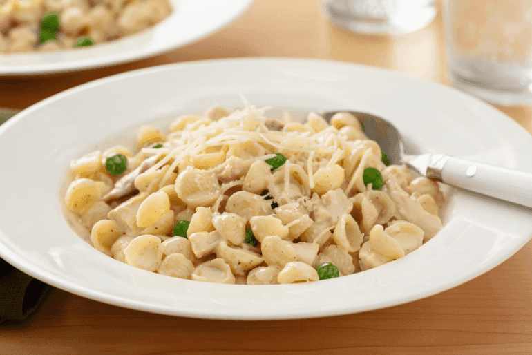 Creamy chicken pasta with peas and parmesan in a white bowl with a white spoon.