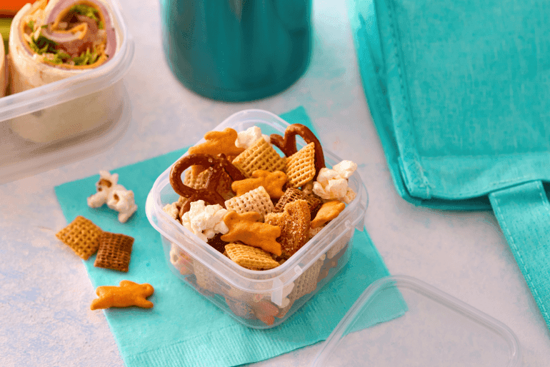 Snack mix in a clear container. Annies Cheddar Bunnies, Pretzels, Chex and Popcorn.